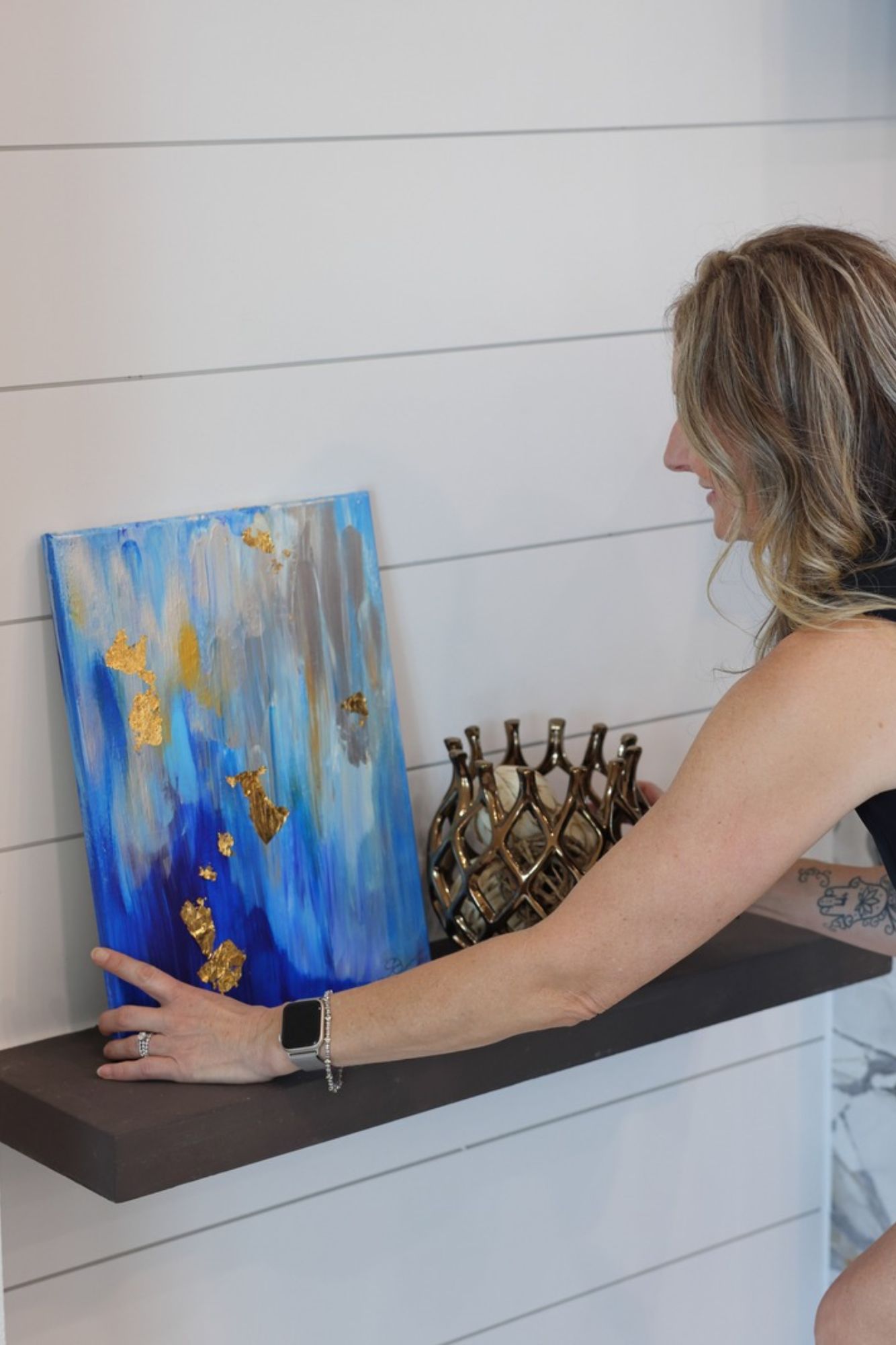 Sara Chiarilli, founder of Artful Conceptions, standing in front of a selection of design choices, including fabric swatches and color samples. She is smiling and engaged, showcasing her creative process and dedication to helping clients bring their design visions to life with personalized and thoughtful selections.