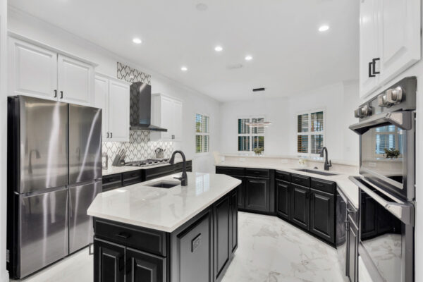 The image shows an open-concept kitchen with a modern and inviting design. The space is spacious, with a large central island that serves as both a prep area and a gathering spot. The kitchen features sleek cabinetry, likely in neutral tones such as white, gray, or wood finishes, with clean lines for a contemporary feel. There may be high-end appliances integrated into the design, such as a built-in oven or refrigerator. The countertop could be made of quartz or granite, offering both durability and style. The open layout seamlessly connects the kitchen to the surrounding living or dining areas, promoting a flow that enhances social interaction and functionality. Natural light likely floods the space, contributing to a bright and airy atmosphere.