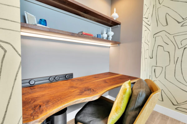 Modern built-in study space featuring custom cabinetry with open shelving and closed storage. The clean, minimalist design includes a spacious desk area, with a comfortable chair and soft lighting. The light-colored wood finishes complement the neutral tones of the room, creating a calm and functional workspace. Above the desk, shelves are neatly organized with books and decorative items, adding both style and practicality to the space.