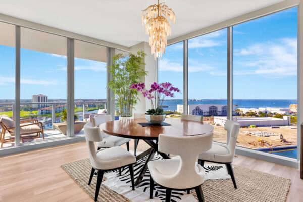 Modern dining area featuring a sleek, wooden dining table surrounded by stylish, upholstered chairs. The space is brightened by large windows that allow natural light to fill the room. Above the table, a contemporary light fixture with clean lines adds an elegant touch. The neutral color palette of the furniture and walls is complemented by subtle decor elements, creating a sophisticated yet inviting dining environment.