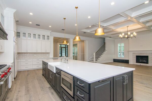 Open-concept kitchen with a gray island featuring a marble countertop and pendant lighting overhead. The island overlooks a cozy living area with a modern fireplace surrounded by built-in shelves, creating a seamless flow between the spaces. Neutral tones and natural light enhance the contemporary design.