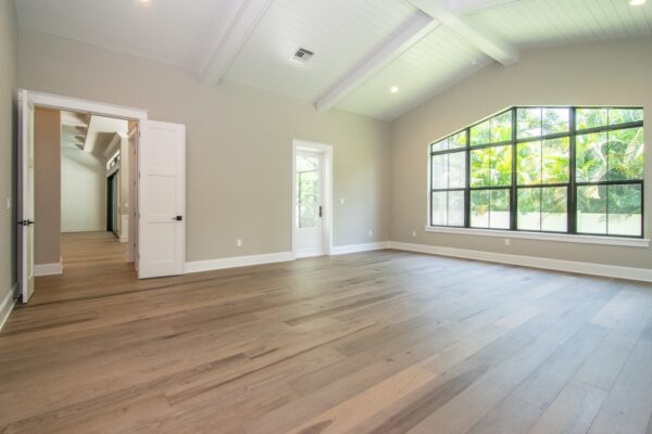 Spacious master bedroom featuring a large window that fills the room with natural light. The room is styled with a neutral color palette, a comfortable bed with soft bedding, and a modern nightstand. The clean, minimalist design creates a peaceful and inviting atmosphere.