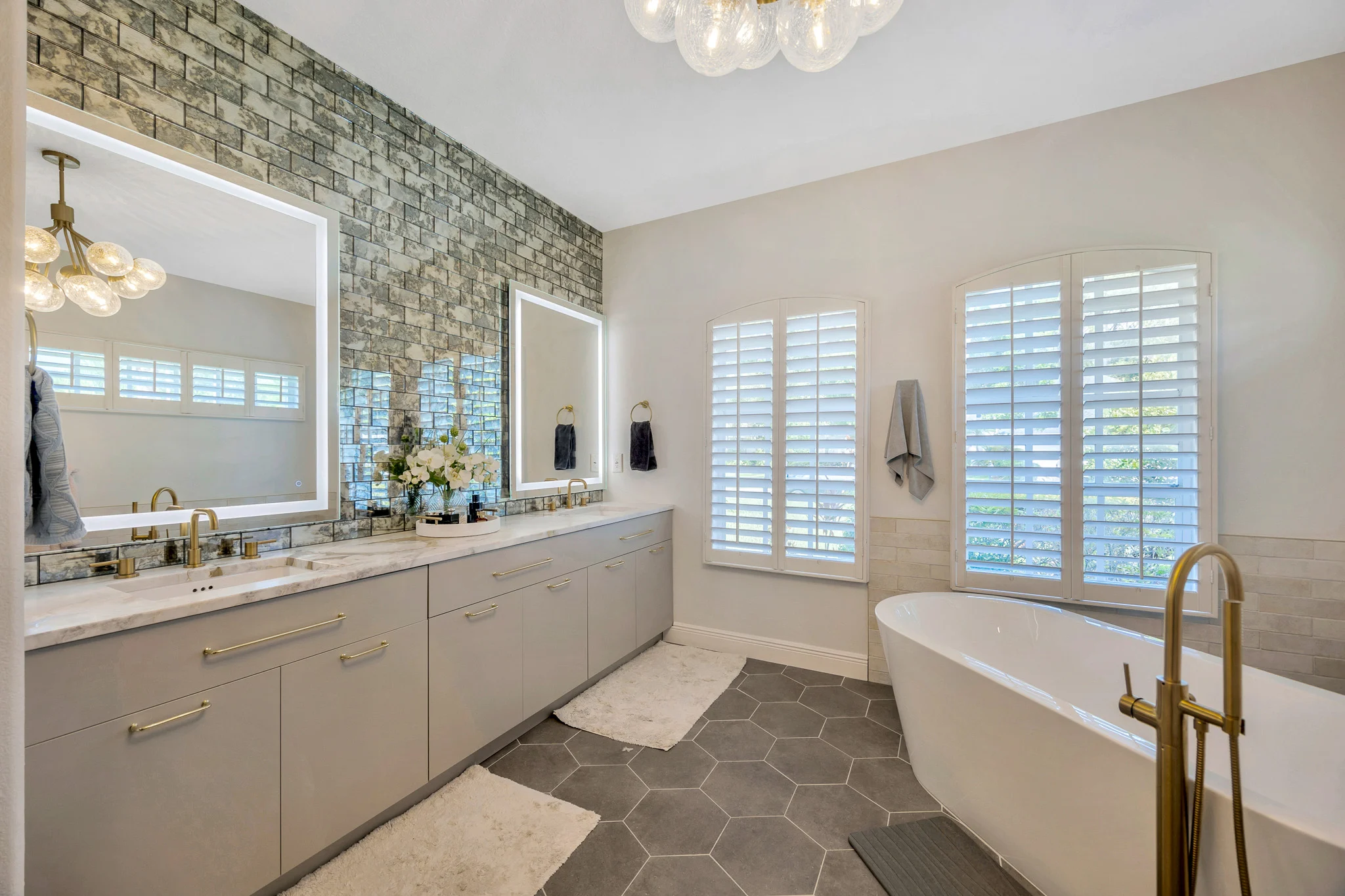 Luxury primary bathroom with custom double vanity, illuminated mirrors, freestanding soaking tub, designer tile accent wall, and gold fixtures.