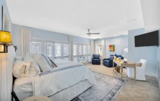 Spacious waterfront primary suite with custom furnishings, sitting area, plantation shutters, and coastal inspired design.