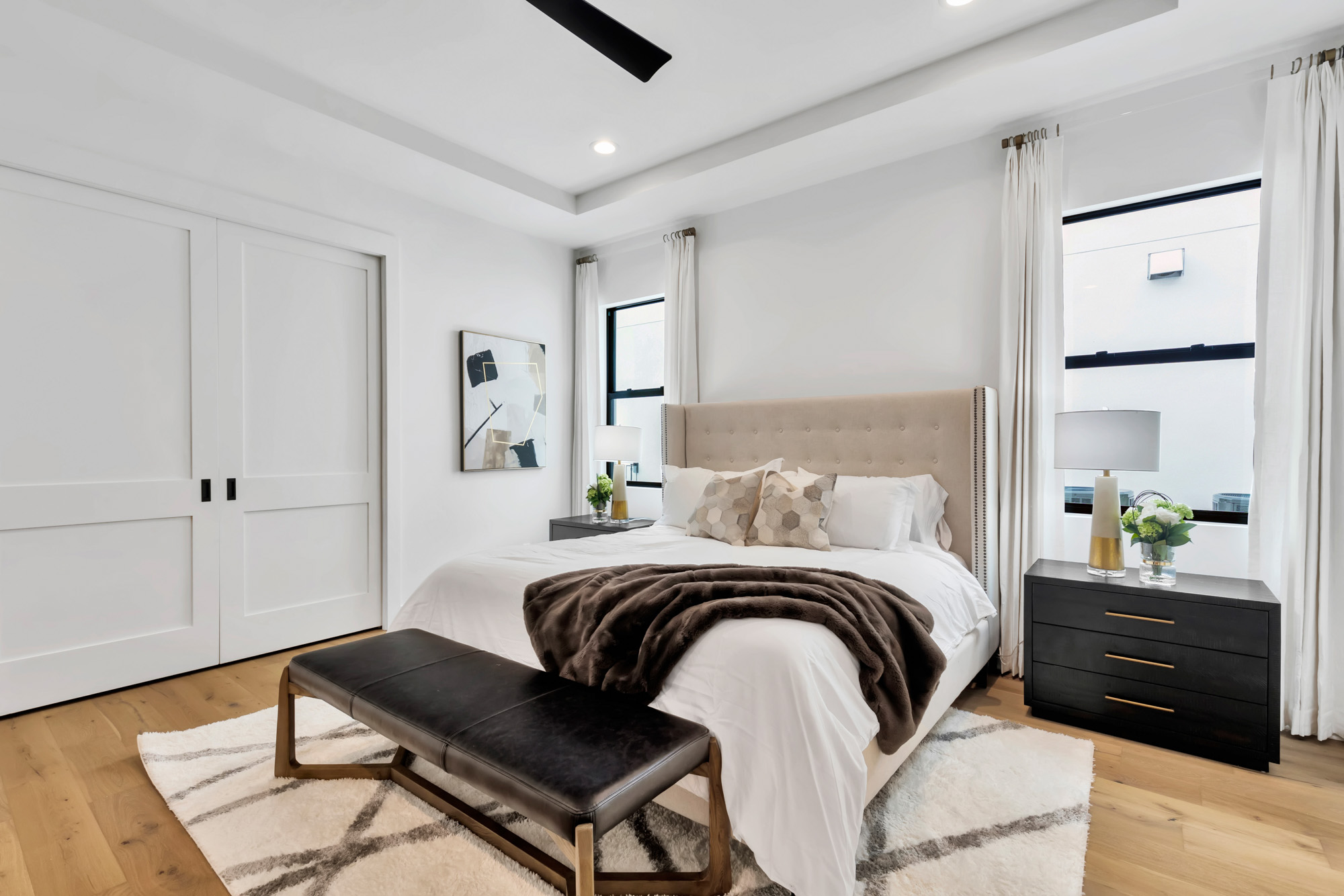 A serene bedroom featuring a linen upholstered headboard that adds a soft, textured element to the space. The bed is complemented by a sleek black nightstand, providing a modern contrast to the light tones of the room. The minimalist design and neutral color palette create a calm and cozy atmosphere, perfect for relaxation.
